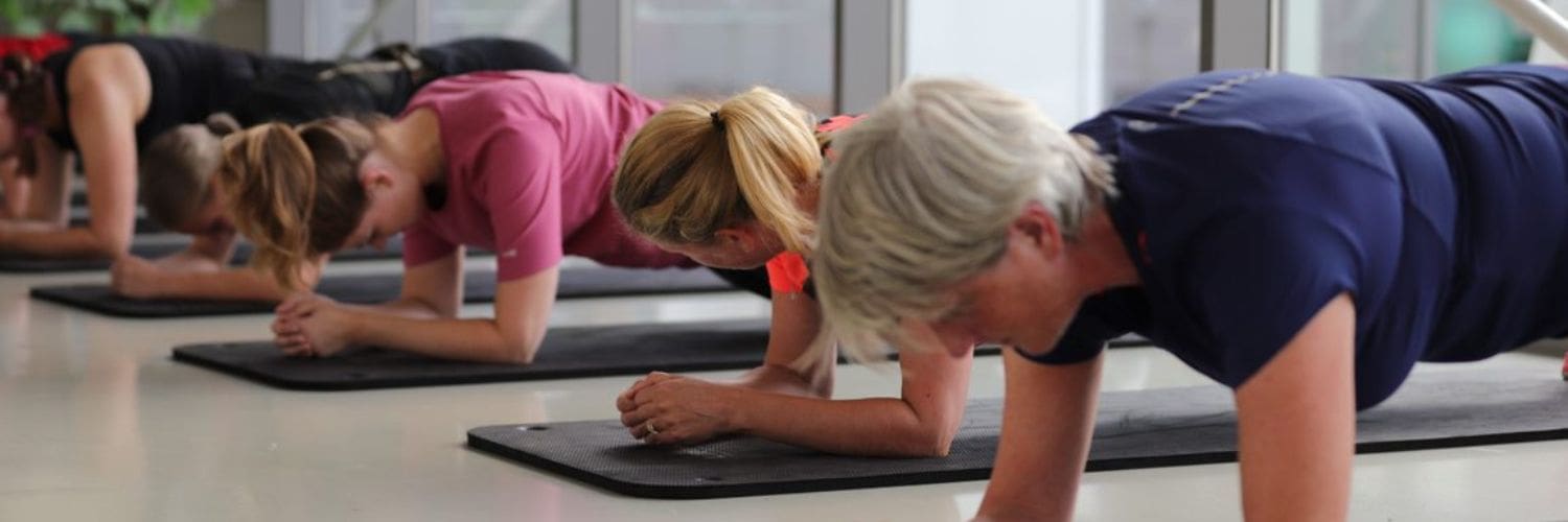 groep vrouwen doet oefening liggend op de vloer, leukend op de ellebogen.