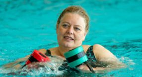 Dame met een rode en groene foam dumbell in het diepe zwembad