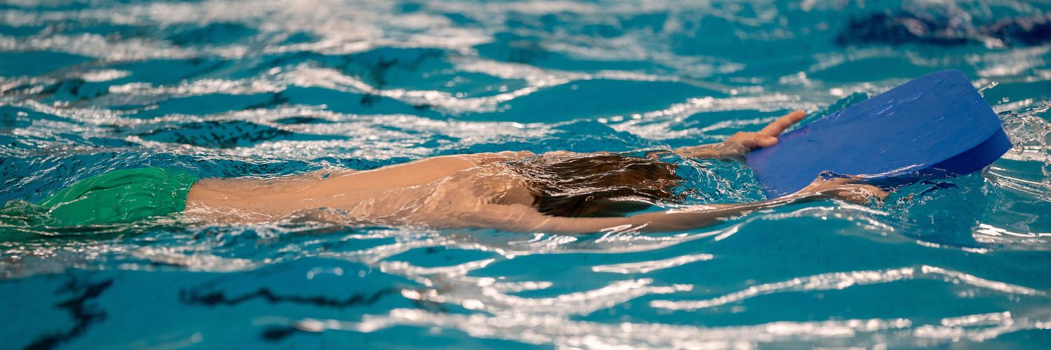 jongen zwemt onder water, armen gestrekt vooruit en houdt een blauw zwemplankje vast