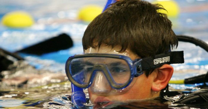 jongen met een duikbril en snorkel steekt net met zijn ogen boven het water van het zwembad uit.