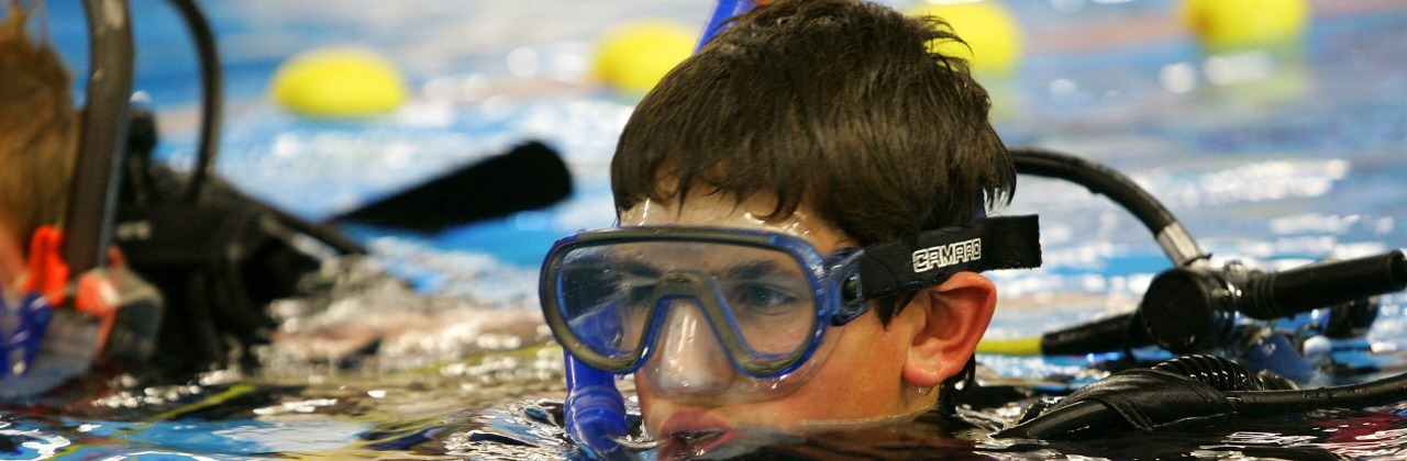 jongen met een duikbril en snorkel steekt net met zijn ogen boven het water van het zwembad uit.