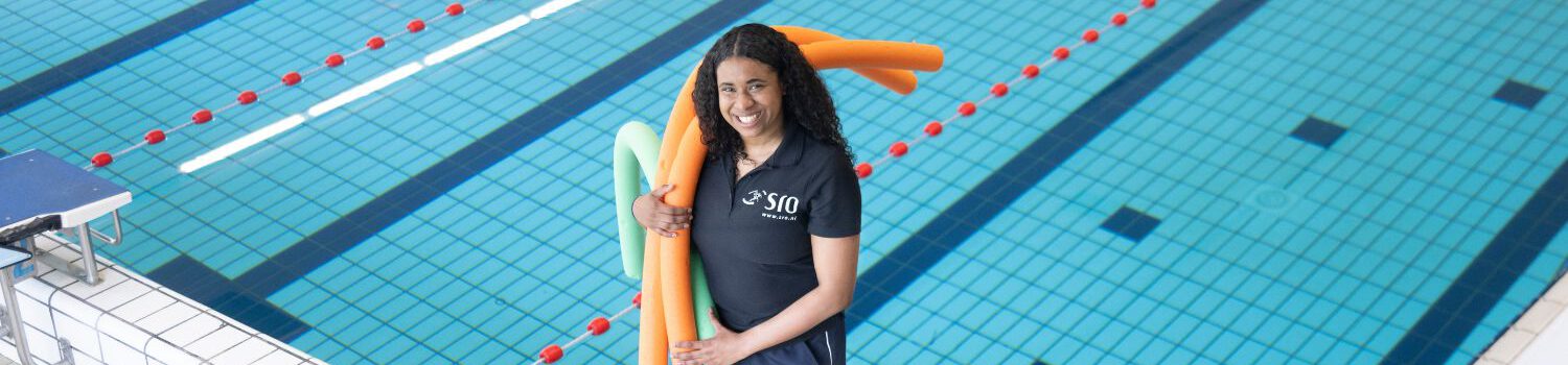 SRO medewerker staat lachend aan de zwembadrand en houdt een aantal poolnoodles in haar hand