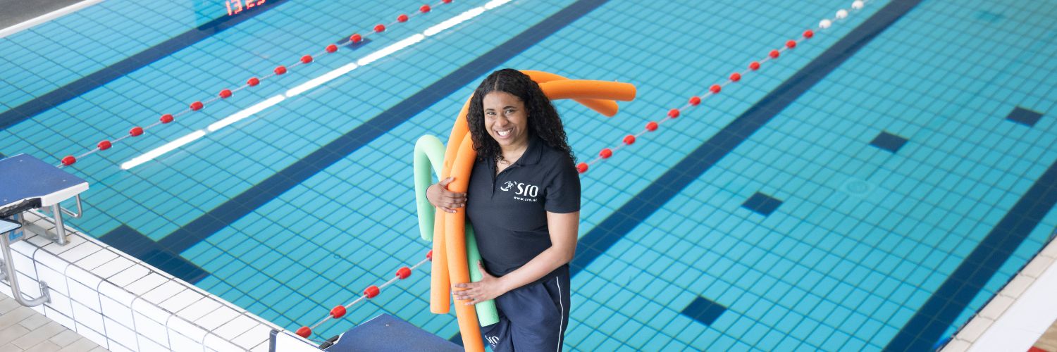 SRO medewerker staat lachend aan de zwembadrand en houdt een aantal poolnoodles in haar hand
