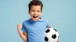 jongetje met voetbal onder arm lacht en trekt arm in omdat hij heeft gescoord